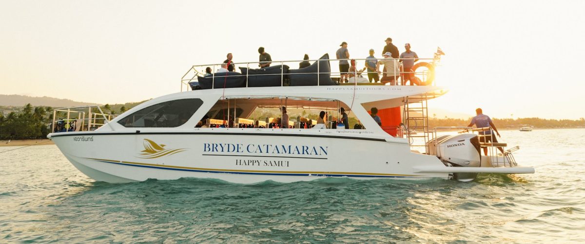 White catamaran on water with passengers at sunset.