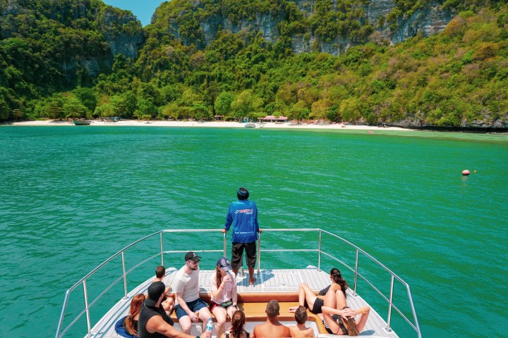 People on a boat approaching a scenic green island beach.