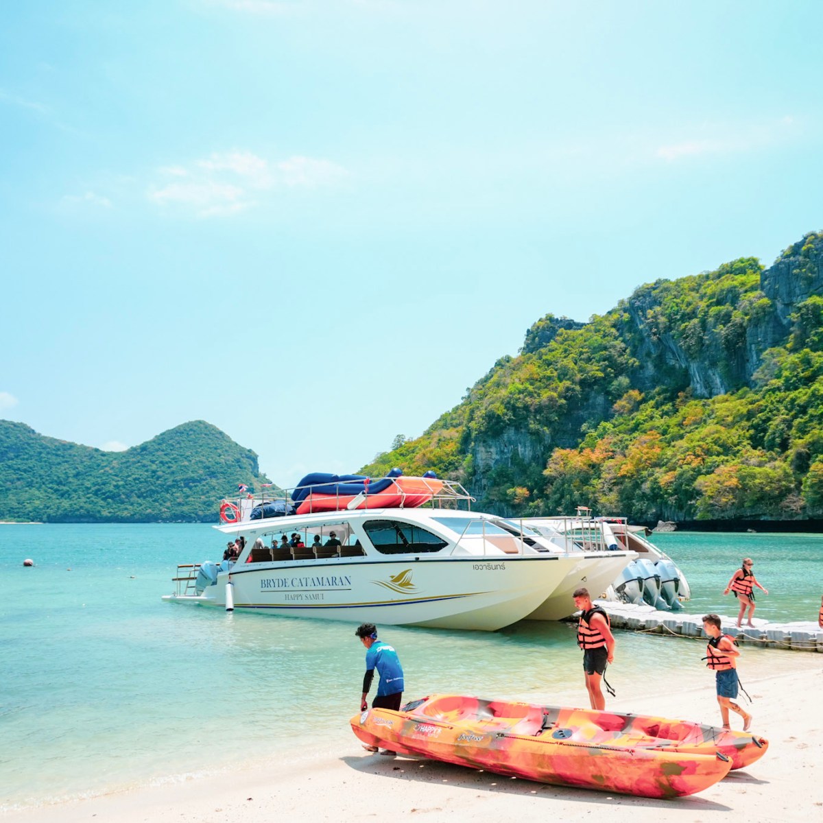 People in life vests on a beach with a boat and distant hills.