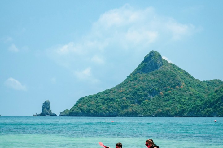 Two people kayaking in turquoise sea near a green island.