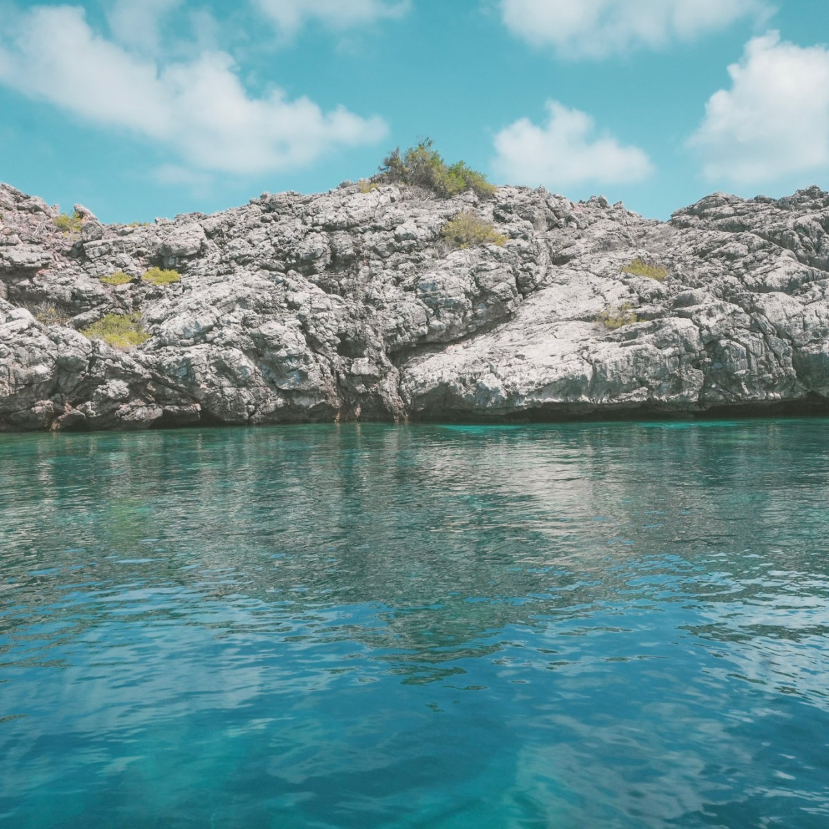 Rocky shoreline with clear blue water under a cloudy sky.
