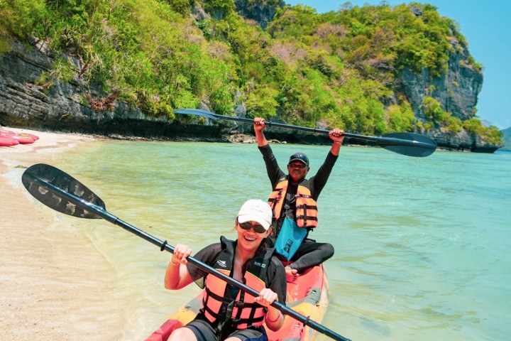 Two people in a kayak on a sunny beach, holding paddles and wearing life vests.
