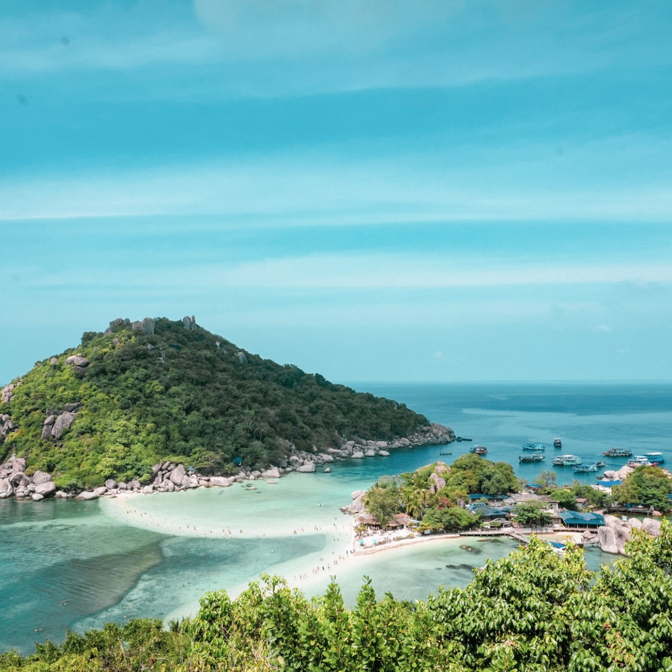 Scenic view of a small island with lush greenery and sandy beaches surrounded by blue ocean.