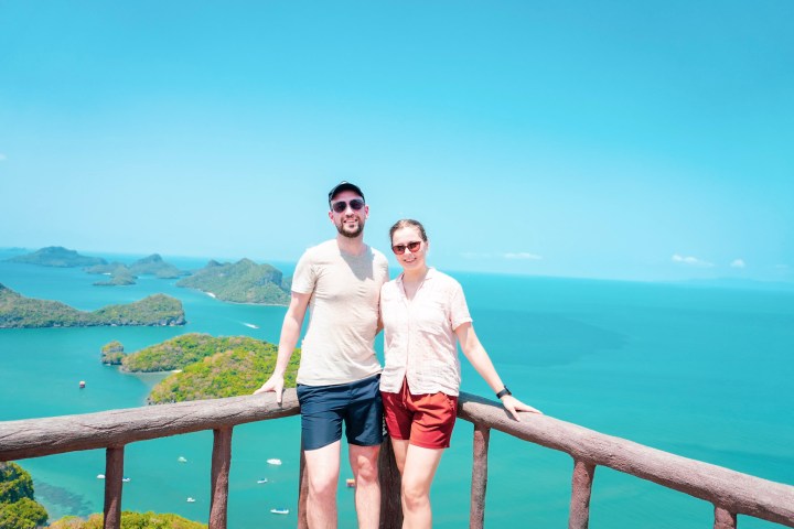 Two people posing by a wooden railing with a scenic ocean view.