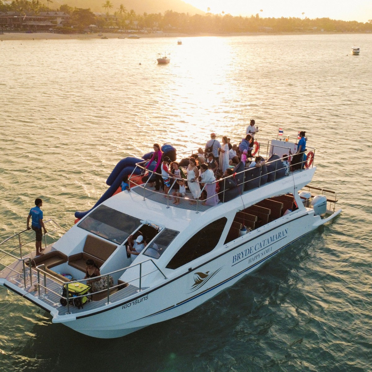 People on a white yacht cruising on a calm body of water at sunset.