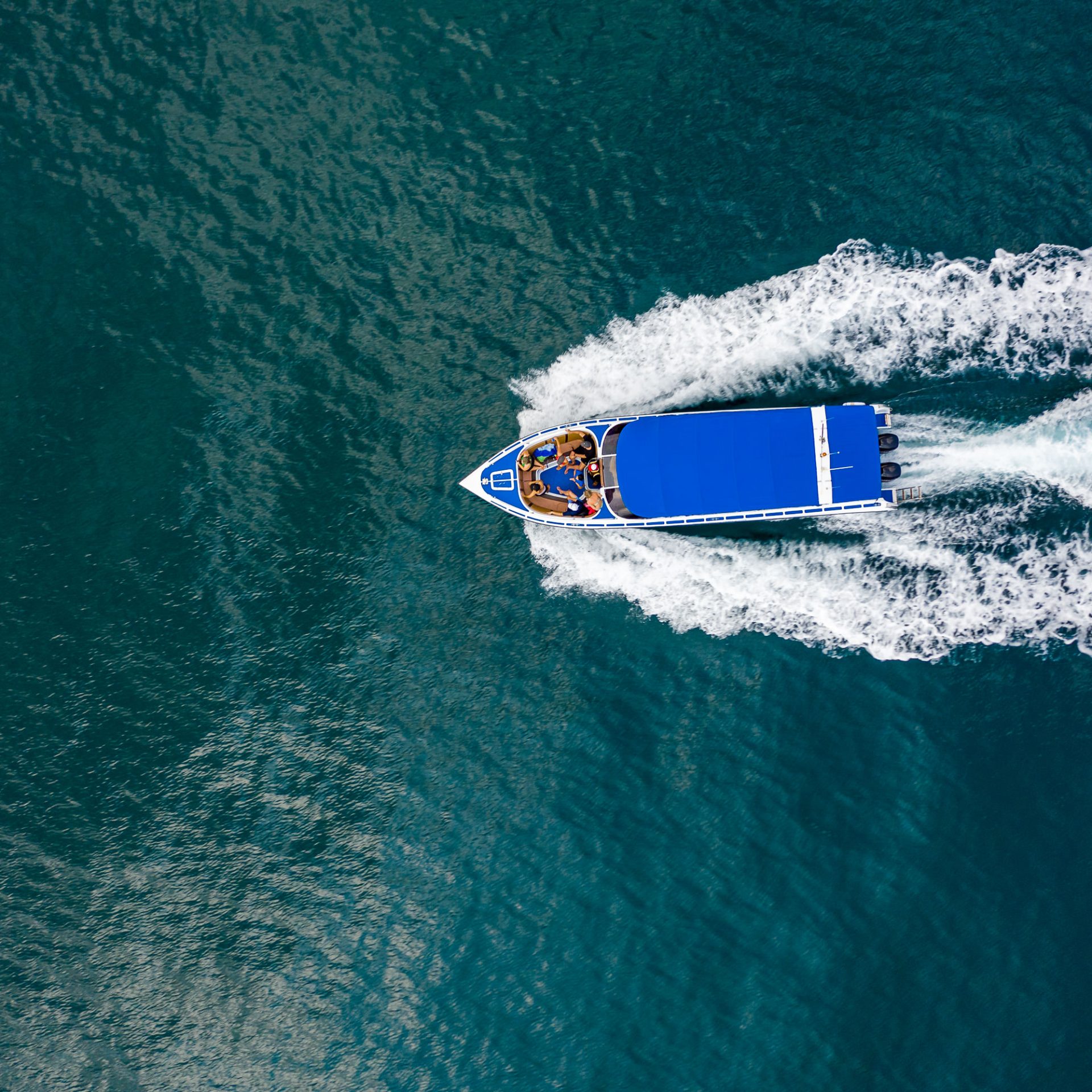 Aerial view of a blue speedboat moving on water, leaving a wake behind.