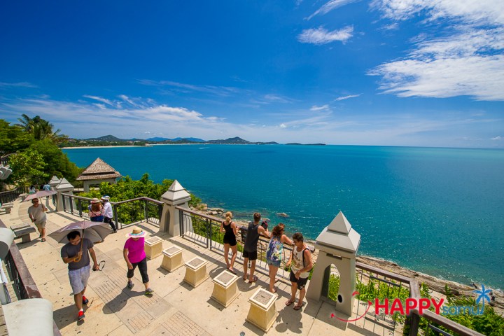 Tourists on a terrace overlooking a blue ocean and clear sky.