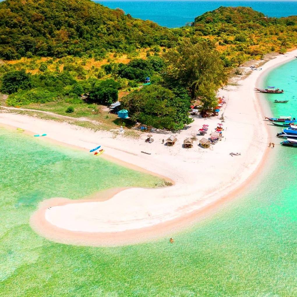 Aerial view of a sandy beach with turquoise water and lush green hills.